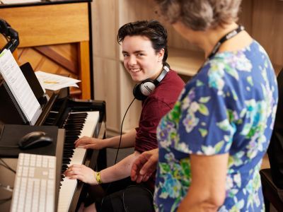 A young man at a keyboard smiling at the teacher.